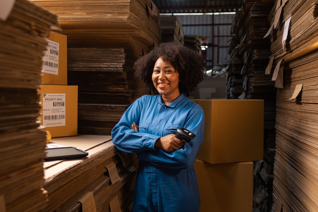 Woman worker surrounded by boxes in a warehouse holding a barcode scanner.