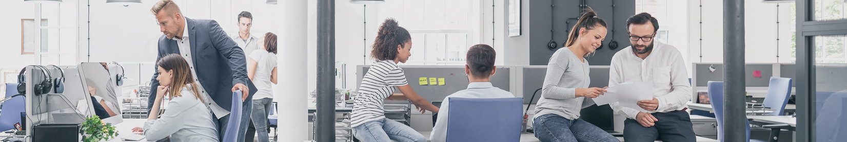 A group of business people sit at desks and talk to one another.