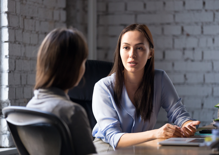 A woman with brown hair consults with another woman.