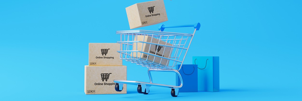 Animated image of a shopping cart with boxes tumbling into it from the air and blue shopping bags beside the cart.